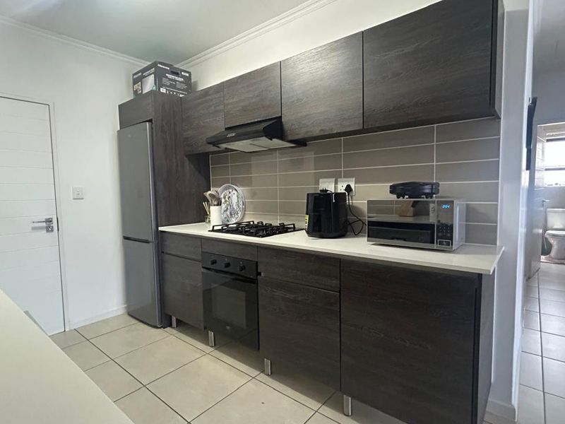 Modern kitchen featuring dark wood grain cabinetry, stone countertops, built-in oven, gas hob, and a tiled backsplash, with adjacent access to the bathroom.