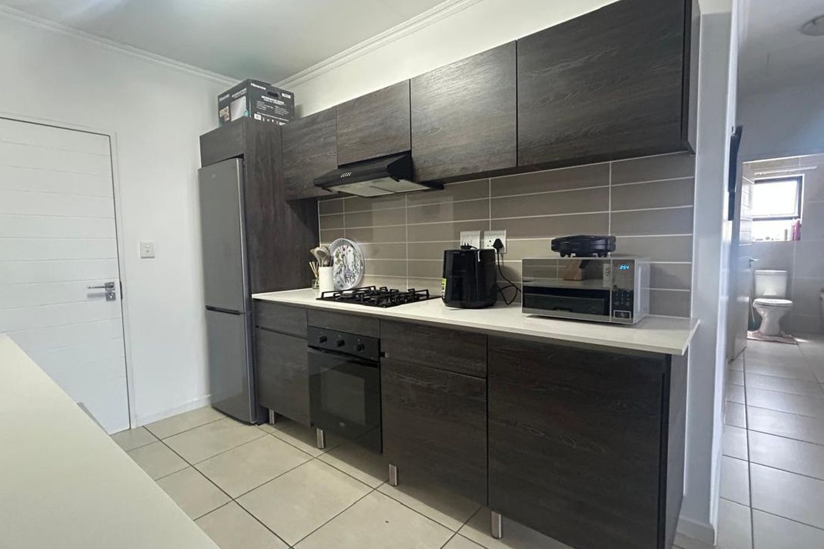 Modern kitchen featuring dark wood grain cabinetry, stone countertops, built-in oven, gas hob, and a tiled backsplash, with adjacent access to the bathroom.