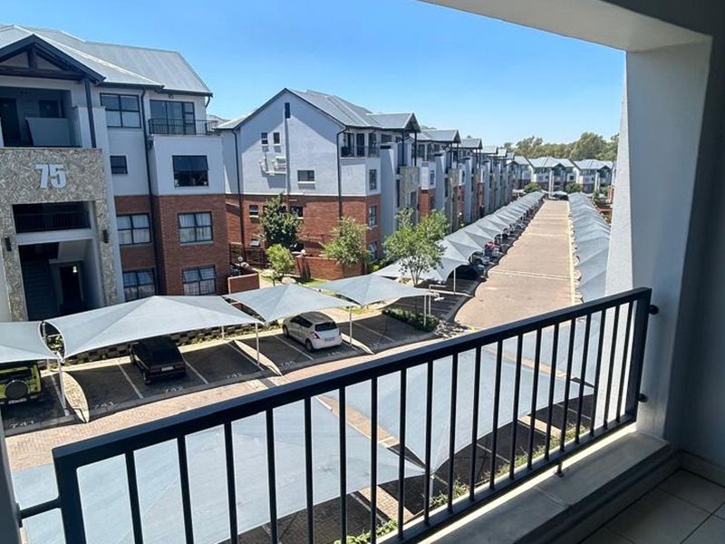 A view from a balcony overlooking the apartment complex parking area with shade-net carports.