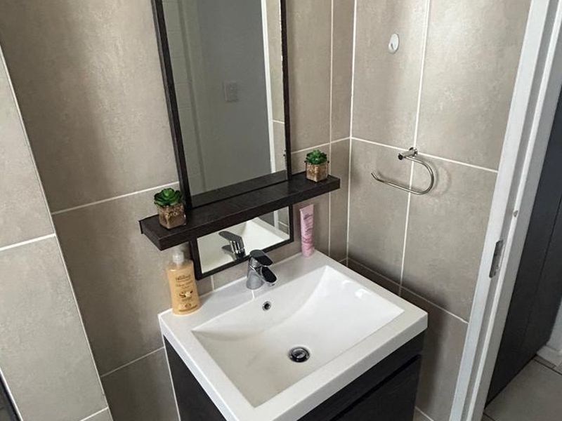 A modern bathroom featuring a vanity cabinet with a ceramic basin, chrome mixer tap, and wall-mounted mirror, complemented by neutral tiled walls and flooring.