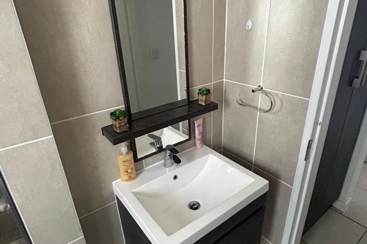 A modern bathroom featuring a vanity cabinet with a ceramic basin, chrome mixer tap, and wall-mounted mirror, complemented by neutral tiled walls and flooring.