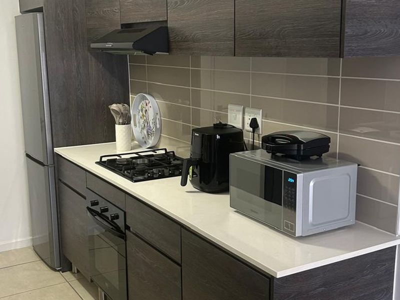 Modern kitchen featuring dark wood-grain cabinetry, stone countertops, a gas hob, built-in oven, and a sleek tiled backsplash.