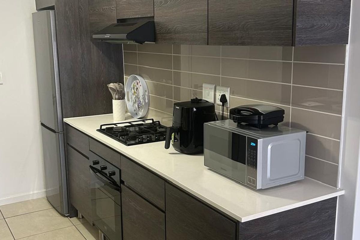 Modern kitchen featuring dark wood-grain cabinetry, stone countertops, a gas hob, built-in oven, and a sleek tiled backsplash.