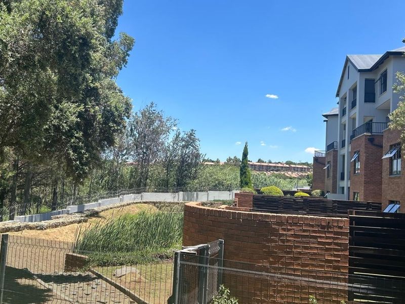 Rear view of the apartment complex featuring brick facade, private balconies, and landscaped grounds with security fencing.