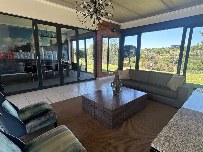 Spacious living area featuring exposed brick walls, large glass sliding doors providing natural light, and a modern chandelier, overlooking a scenic outdoor landscape.