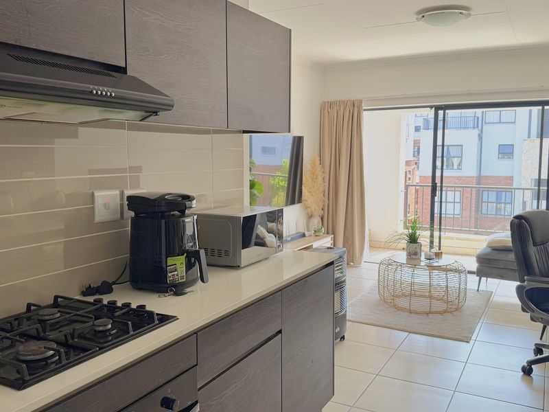 Modern open-plan kitchen and living area featuring dark wood cabinetry, gas hob, tiled flooring, and direct access to a private balcony.