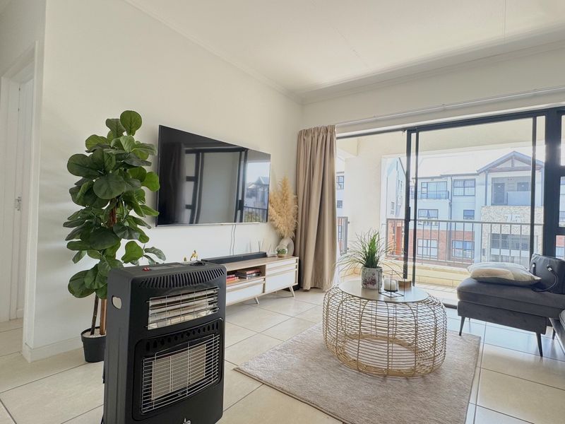 A bright living room featuring neutral tiled flooring and a large sliding glass door providing access to the balcony.