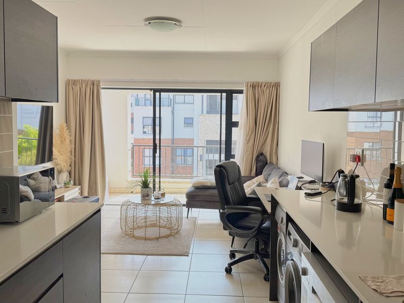 Modern open-plan apartment featuring a sleek kitchen with stone countertops and tiled flooring, seamlessly flowing into a living area with balcony access.