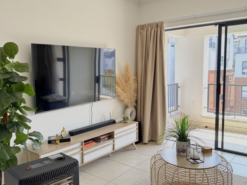 A bright living room featuring tiled flooring and a large sliding glass door that provides access to an outdoor balcony area.