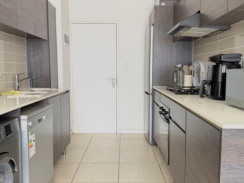 Modern galley-style kitchen featuring dark wood-grain cabinetry, stone countertops, tiled backsplash, and integrated gas hob with extractor fan.