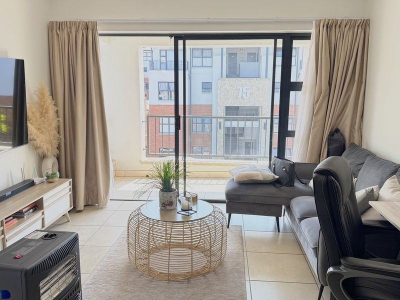 A bright living room featuring tiled flooring and large sliding glass doors that provide access to a private balcony.