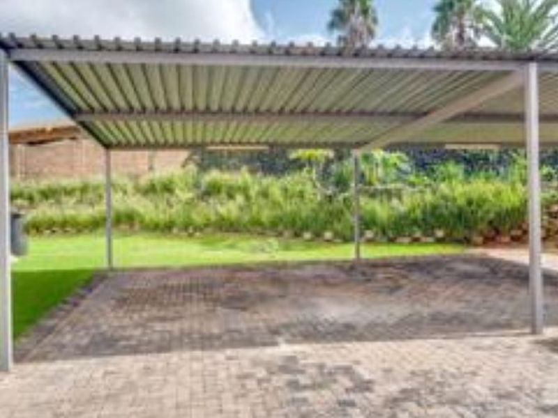 A functional outdoor carport with a metal roof and paved driveway, providing covered parking space adjacent to the property's garden area.