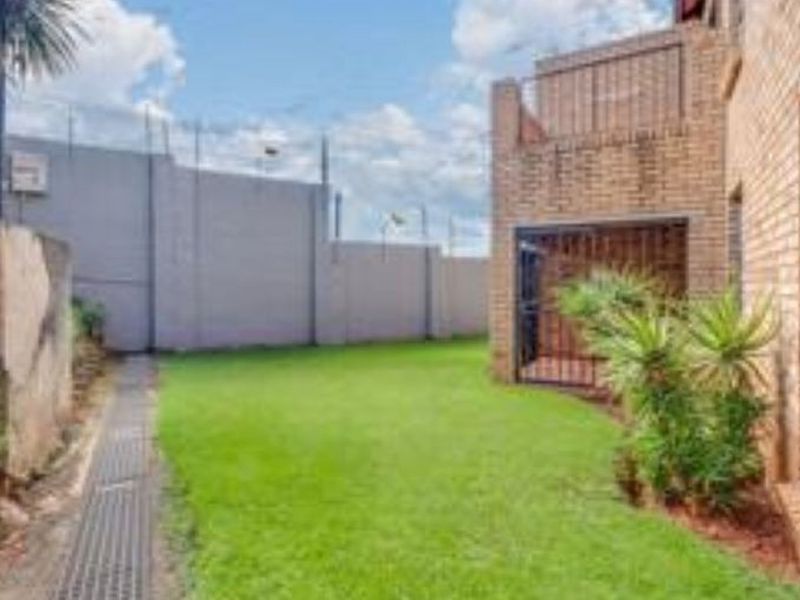 A private rear garden area featuring a well-maintained lawn, brick townhouse facade, and secure perimeter walling.