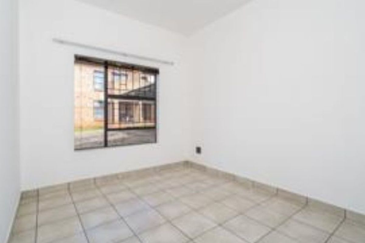 A vacant bedroom featuring neutral tiled flooring and a window fitted with security bars, offering a blank canvas for personalization.