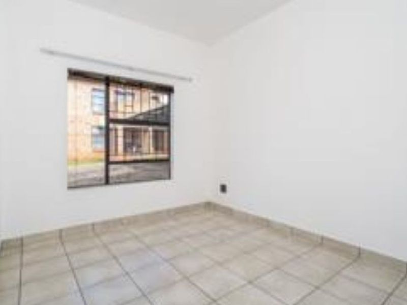 A vacant bedroom featuring neutral tiled flooring and a window fitted with security bars, offering a blank canvas for personalization.