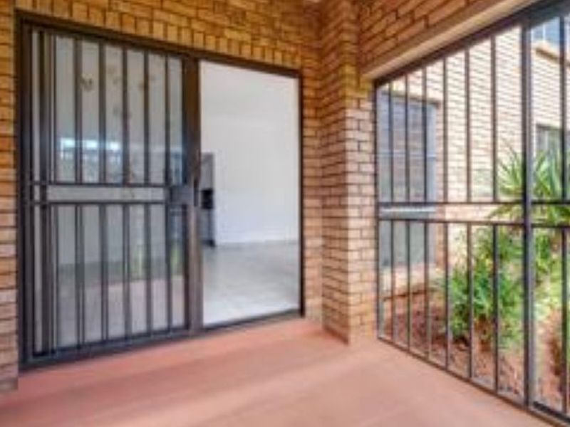 A covered patio area featuring face-brick walls, tiled flooring, and secure metal sliding gates leading into the interior living space.