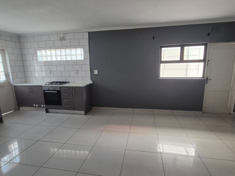 A clean, modern kitchen featuring dark cabinetry, a gas hob, built-in oven, and white tiled flooring with a subway tile backsplash.