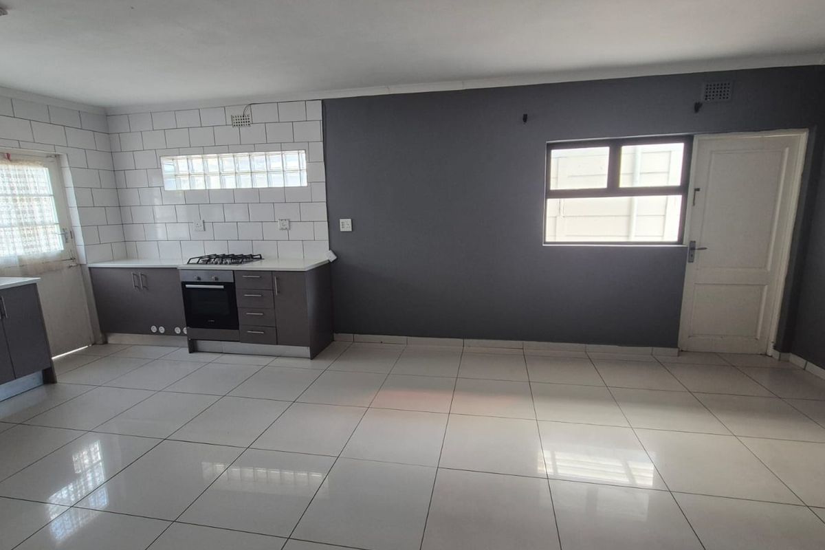 A clean, modern kitchen featuring dark cabinetry, a gas hob, built-in oven, and white tiled flooring with a subway tile backsplash.