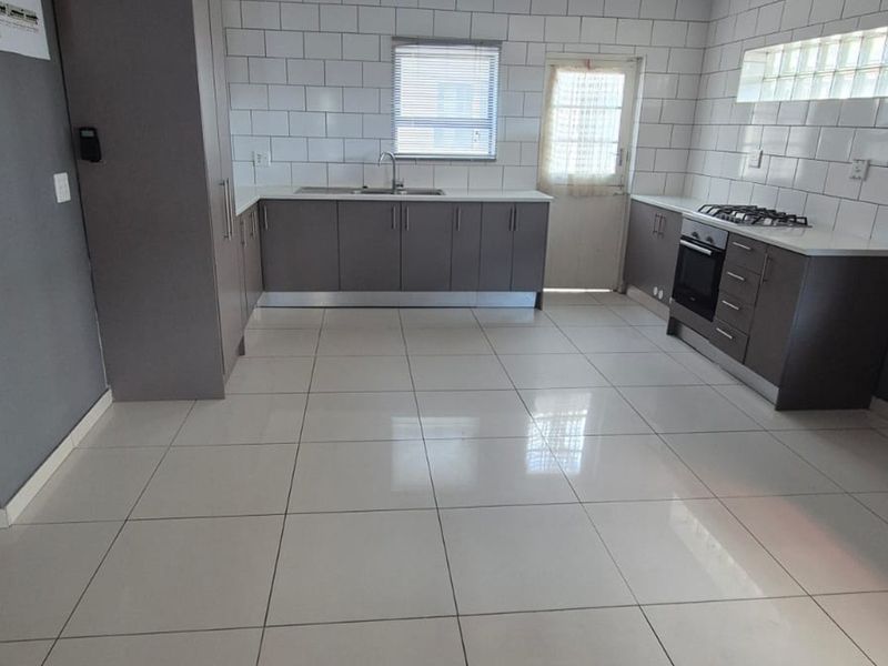 Modern kitchen featuring grey cabinetry, subway tile backsplash, built-in oven, gas hob, and neutral tiled flooring in an open-plan layout.