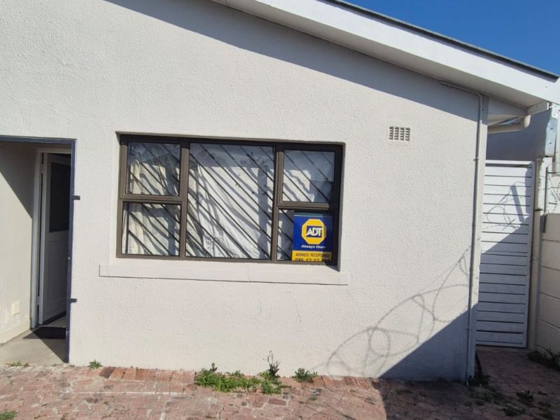 Rear exterior view of the property featuring a security gate, aluminium window, and paved courtyard area with perimeter walling.