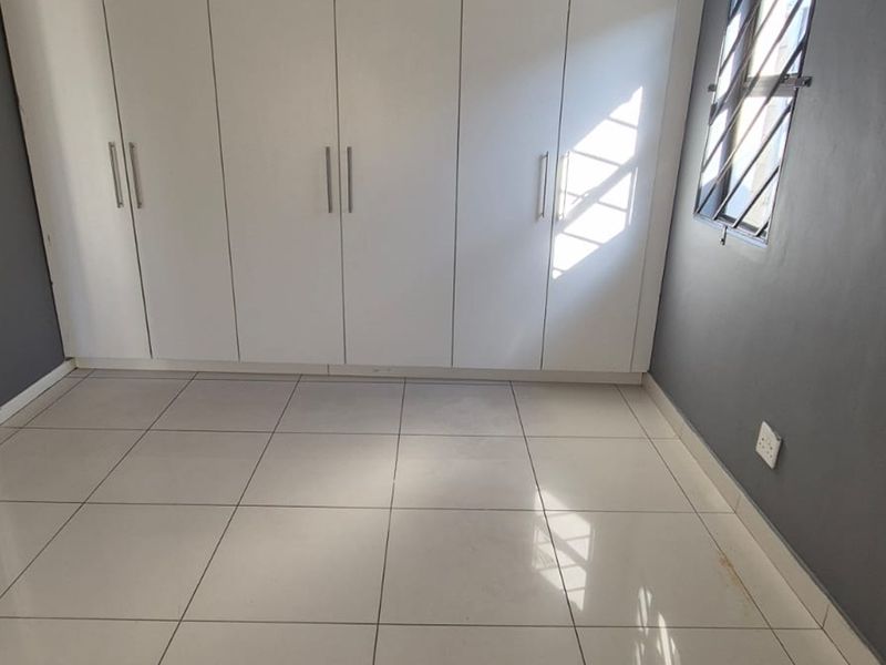 A clean, empty bedroom featuring neutral tiled flooring, dark grey walls, and ample built-in cupboard storage with modern white doors.