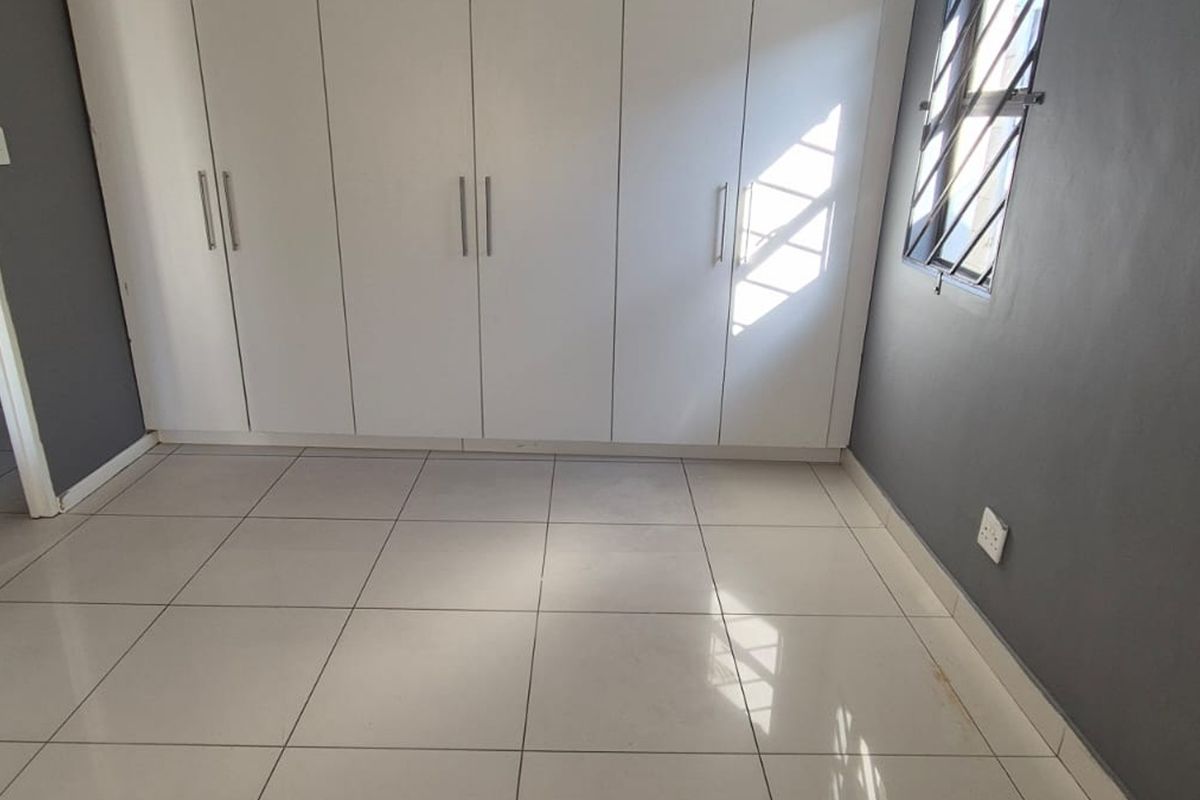 A clean, empty bedroom featuring neutral tiled flooring, dark grey walls, and ample built-in cupboard storage with modern white doors.