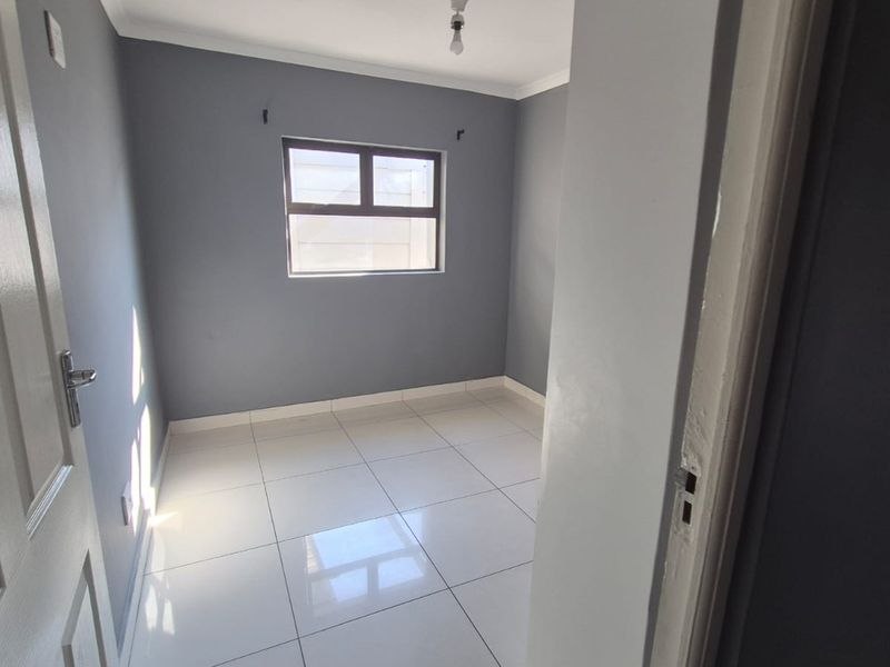 A clean, empty bedroom featuring neutral grey walls, white tiled flooring, and an aluminium-framed window, providing a blank canvas for personalization.