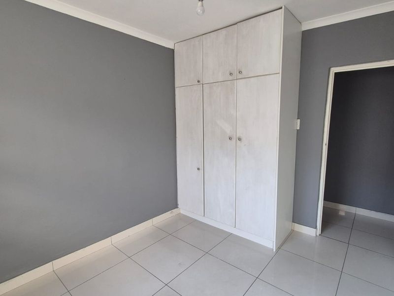 A clean, empty bedroom featuring neutral grey walls, white tiled flooring, and built-in storage cupboards.