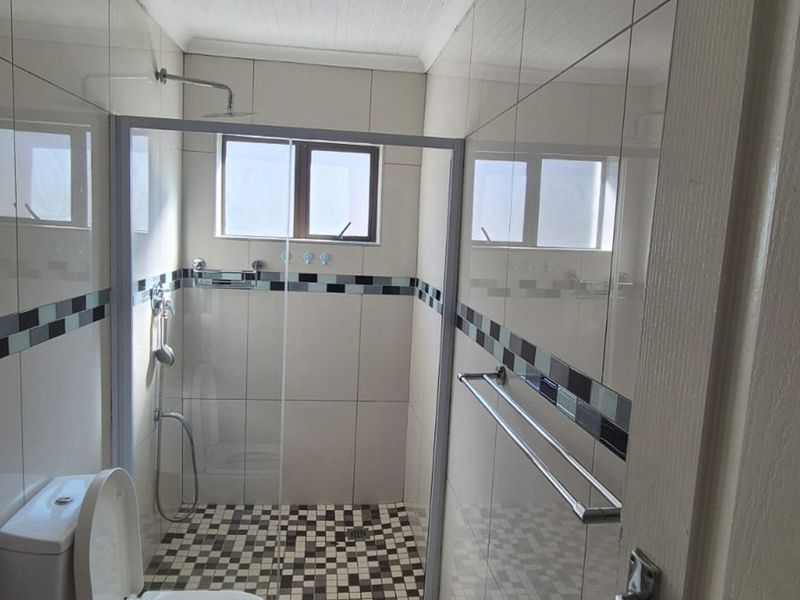 A clean, modern bathroom featuring a walk-in shower with a glass enclosure, mosaic floor tiling, and neutral wall tiles.