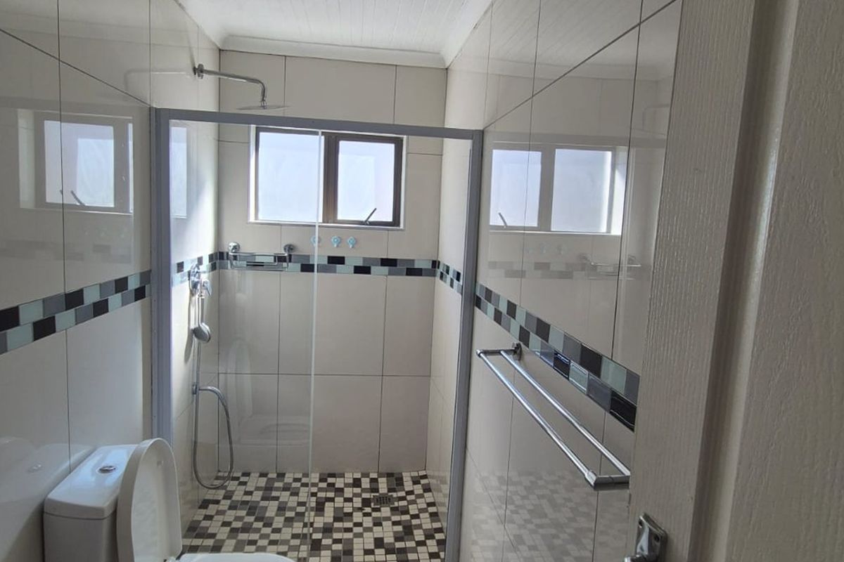 A clean, modern bathroom featuring a walk-in shower with a glass enclosure, mosaic floor tiling, and neutral wall tiles.