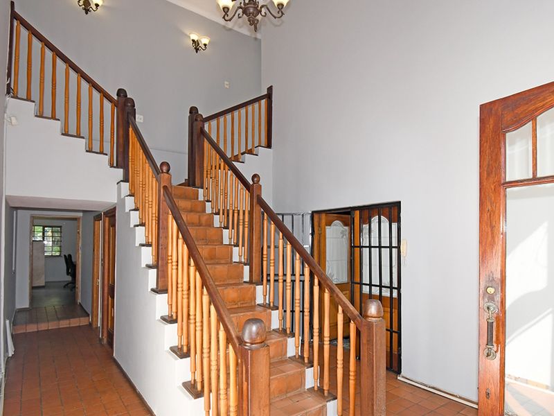 Spacious entrance hall featuring a central timber staircase with wooden balustrades and traditional tiled flooring, providing access to multiple areas of the home.