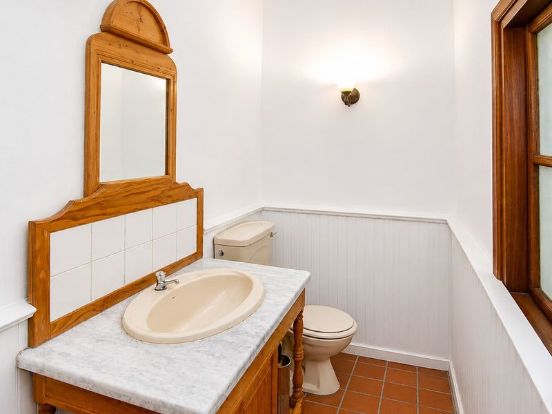 A functional bathroom featuring a vanity with a marble countertop, wainscoting wall paneling, and classic terracotta floor tiles.