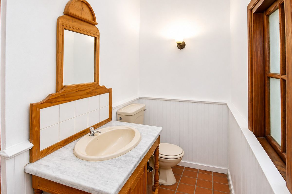 A functional bathroom featuring a vanity with a marble countertop, wainscoting wall paneling, and classic terracotta floor tiles.
