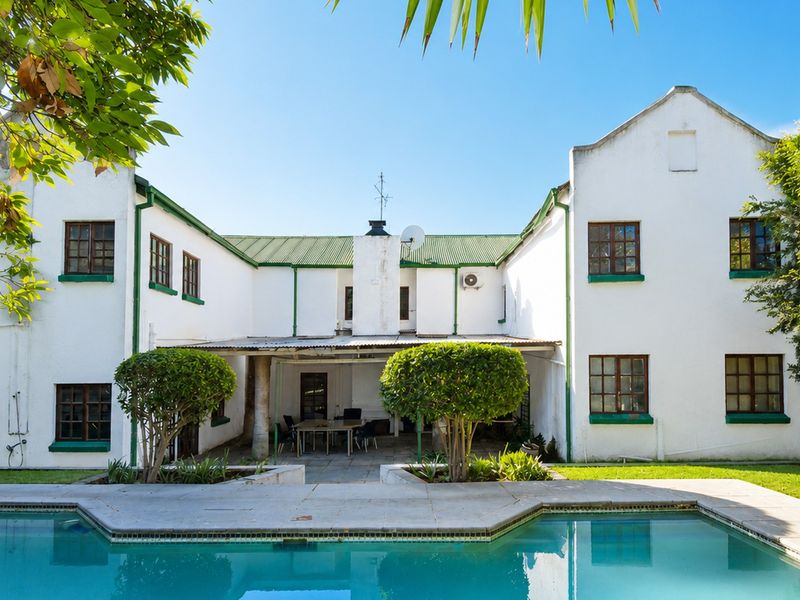 Rear view of the house featuring a swimming pool, a covered patio area, and a white facade with green trim.