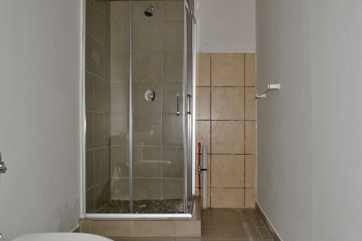 A functional bathroom featuring a tiled shower enclosure and toilet, currently requiring minor cosmetic finishing and paint touch-ups.