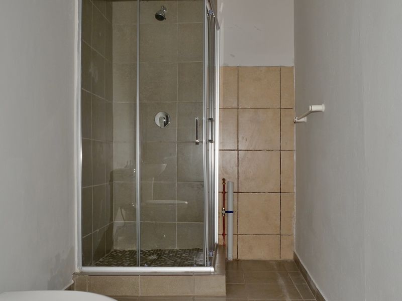 A functional bathroom featuring a tiled shower enclosure and toilet, currently requiring minor cosmetic finishing and paint touch-ups.