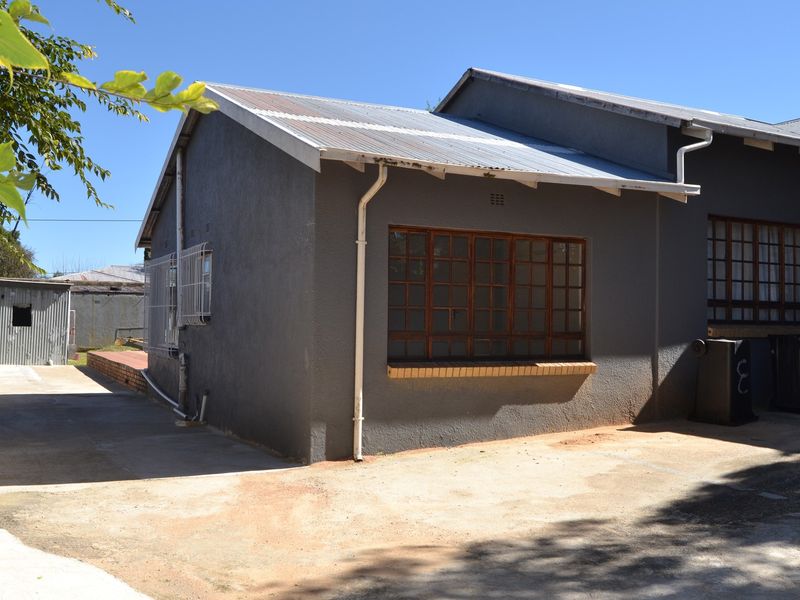 Rear exterior view of the cottage featuring a corrugated metal roof, timber-framed windows with security bars, and a concrete driveway area.
