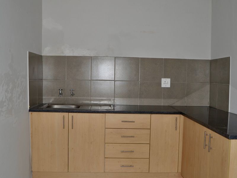A compact kitchen area featuring laminate cabinetry, granite countertops, and a stainless steel sink with tiled splashback, requiring minor wall repairs.