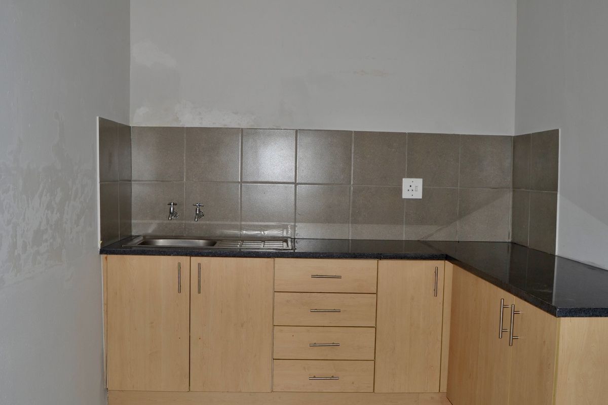 A compact kitchen area featuring laminate cabinetry, granite countertops, and a stainless steel sink with tiled splashback, requiring minor wall repairs.