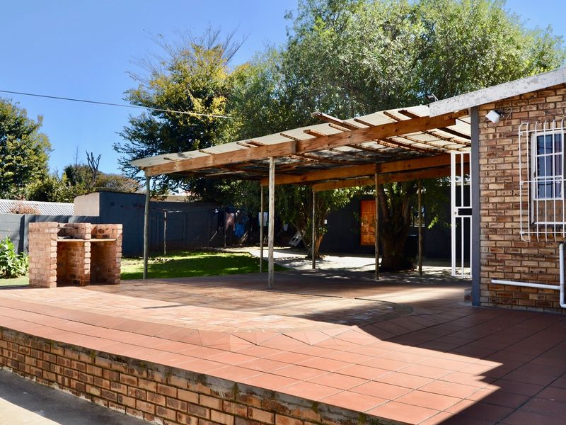 Outdoor patio area featuring a brick built-in braai, tiled flooring, and a timber pergola structure, set within a private backyard space.