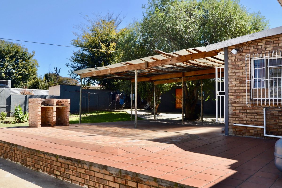 Outdoor patio area featuring a brick built-in braai, tiled flooring, and a timber pergola structure, set within a private backyard space.