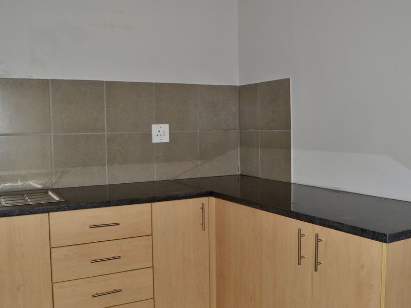 A compact kitchen area featuring light wood-finish cabinetry, dark granite countertops, a stainless steel sink, and a neutral tiled backsplash.