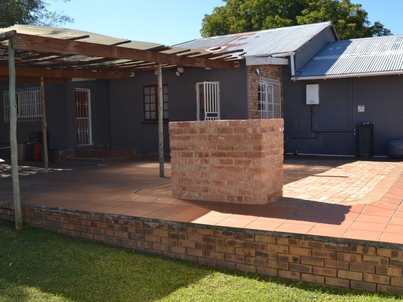 Rear exterior view of the cottage featuring a tiled patio, a brick braai area, and a timber pergola structure.