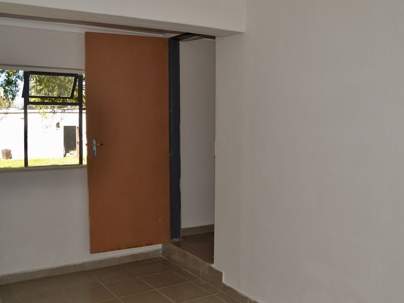 A simple, empty hallway area featuring tiled flooring, a window with garden views, and an internal door leading to an adjacent space.