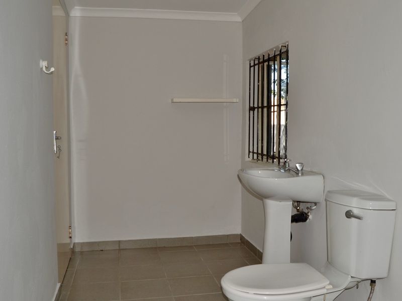 A simple, functional bathroom featuring a pedestal basin, toilet, and tiled flooring, with security bars installed on the window.