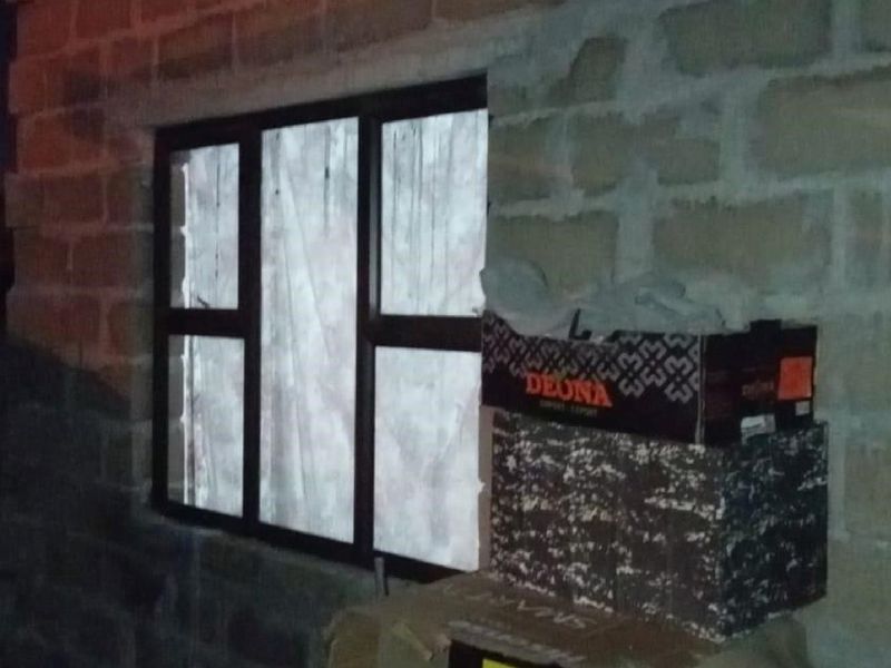 An interior view showing an unfinished exposed concrete block wall and a dark aluminium window frame in a room under construction.