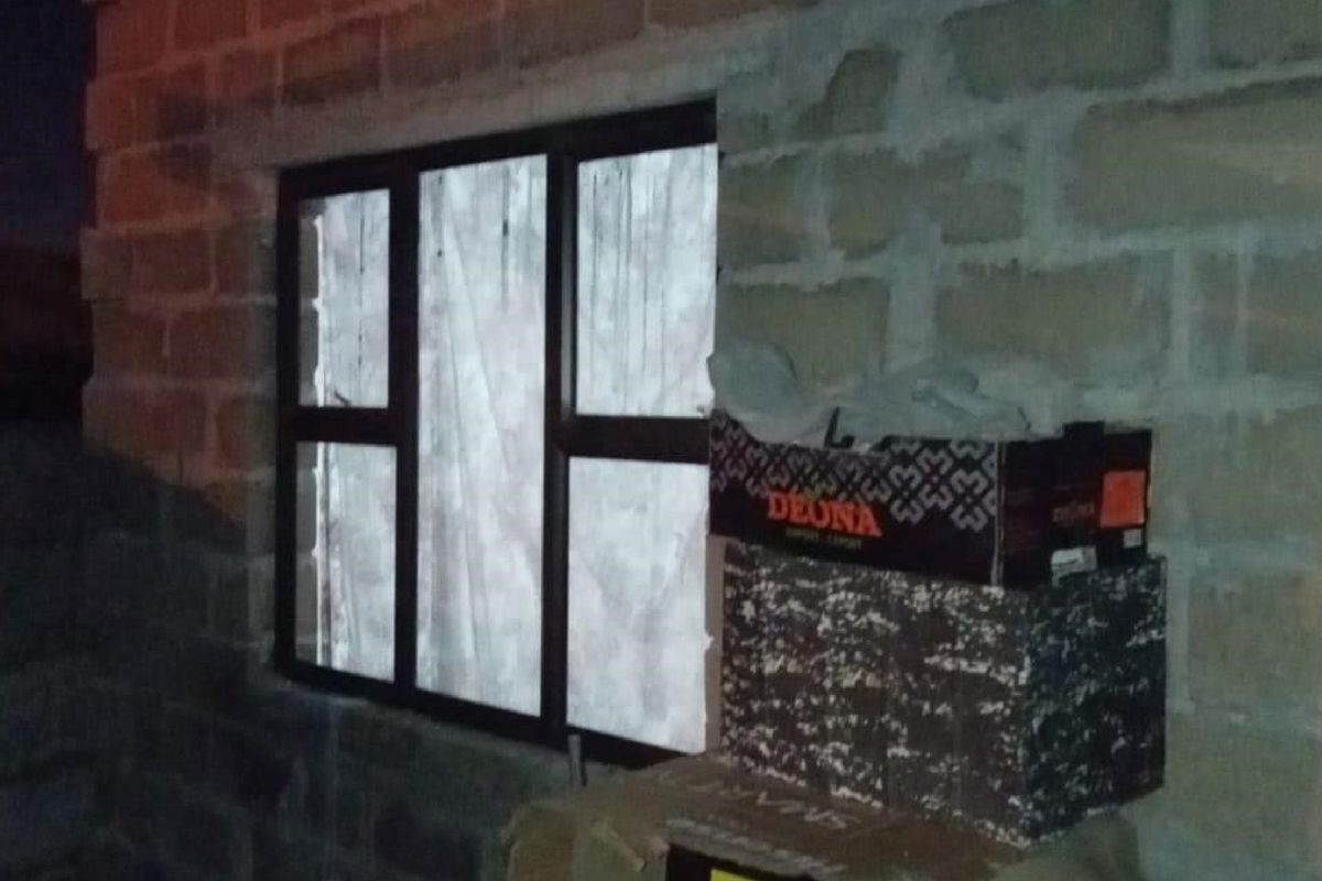 An interior view showing an unfinished exposed concrete block wall and a dark aluminium window frame in a room under construction.