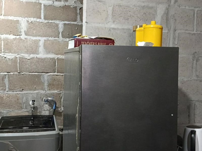 A utility or laundry area featuring exposed concrete block walls and basic plumbing connections, requiring finishing to improve the space's aesthetic and functionality.