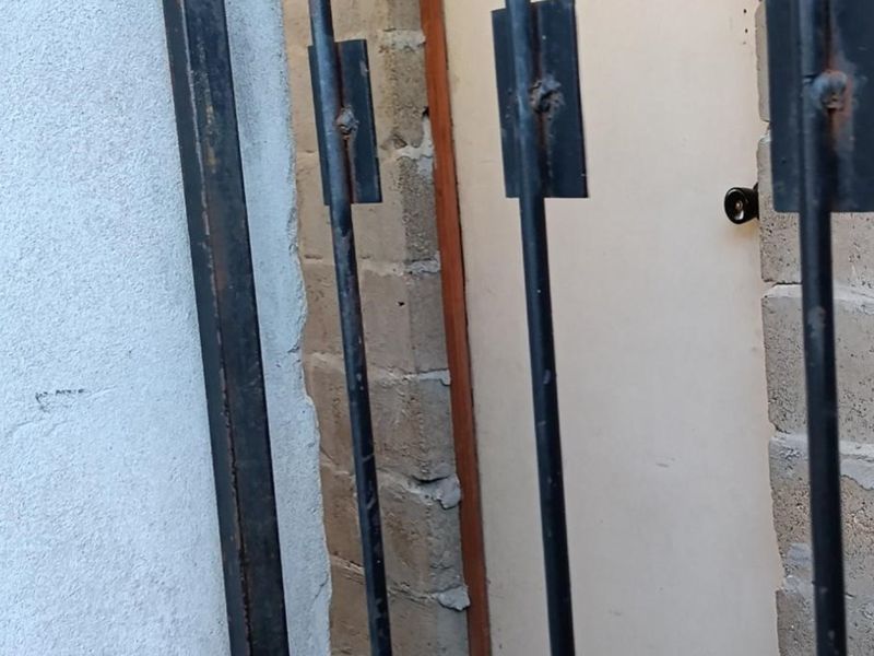 A close-up view of a security gate and entrance area showing signs of wear and unfinished brickwork.