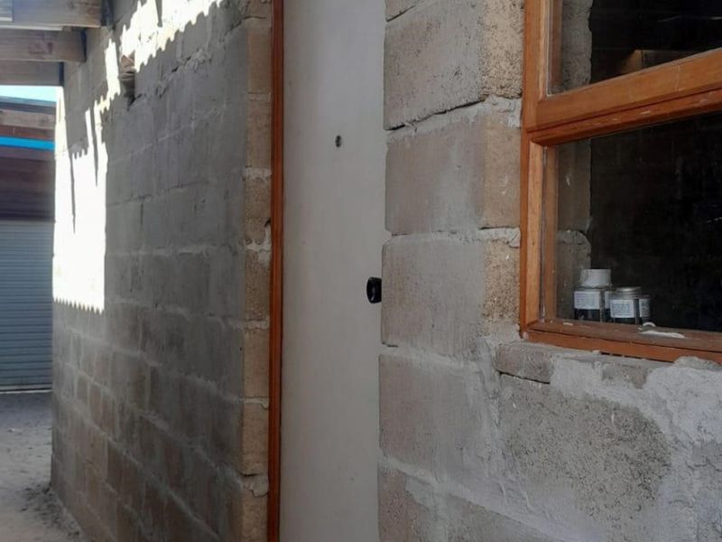 Exterior view of a rear building section featuring exposed concrete block walls, a timber window frame, and a solid entrance door.